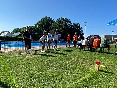 Gruppe an Menschen spielt Kubb vor Schwimmbecken